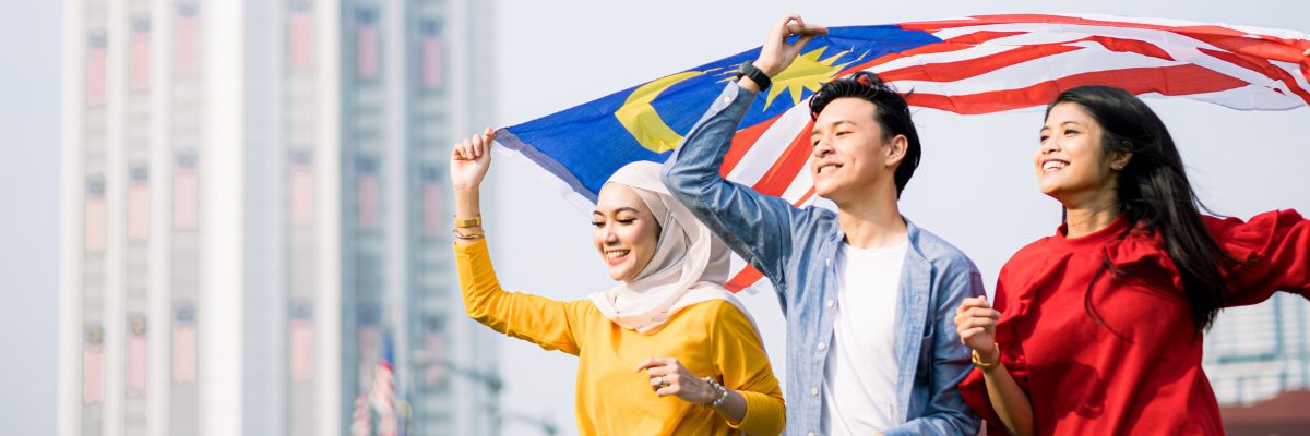 Three smiling people holding the Malaysian flag outdoors.